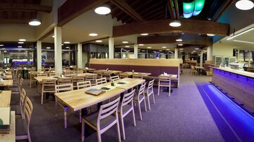 A modern restaurant with stylish wooden tables and chairs. The lighting is warm and creates an inviting atmosphere.