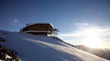 A modern mountain station in a snow-covered landscape. The sun rises behind the mountains, creating a picturesque view.