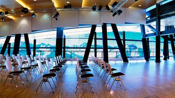 A modern conference room with empty chairs and large windows. The view extends to impressive mountain landscapes.