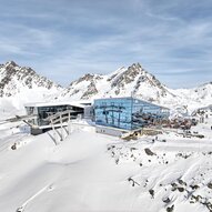 Eine moderne Bergstation in den verschneiten Alpen. Im Hintergrund sind majestätische Berge und ein klarer Himmel zu sehen.