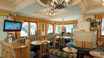 A cozy restaurant with blue and yellow fabrics. Bright windows and a decorative ceiling create an inviting atmosphere.