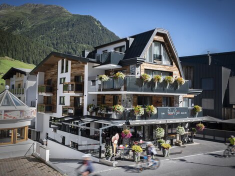 A modern hotel with blooming balcony plants in a mountain landscape. The facade is friendly and inviting.