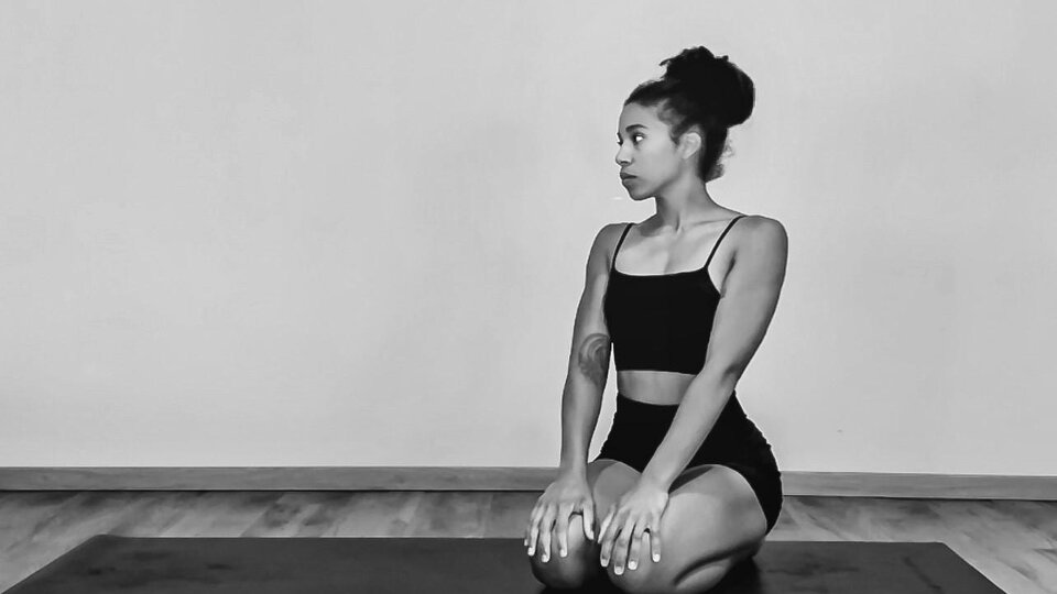 Eine Person sitzt in einer Yogaposition auf einer Matte. Der Raum ist schlicht und minimalistisch.
