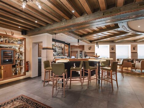 An elegant bar with a wooden ceiling and modern furnishings. Cozy seating and a well-stocked shelf give the atmosphere an inviting character.