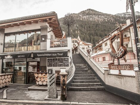 Ein modernes Gebäude mit Holzverkleidung und großen Fenstern. Treppen führen zu einer malerischen Bergkulisse im Hintergrund.