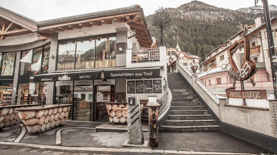 Ein modernes Gebäude mit Holzverkleidung und großen Fenstern. Treppen führen zu einer malerischen Bergkulisse im Hintergrund.