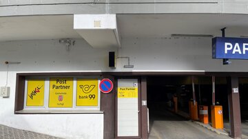 A parking garage with an entrance area that offers postal and banking services. The true partners are clearly marked with yellow signs.