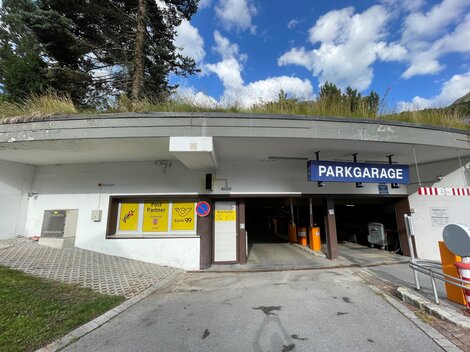 A parking garage with an entrance and a sign that reads "PARKGARAGE". The sky is blue with some clouds.