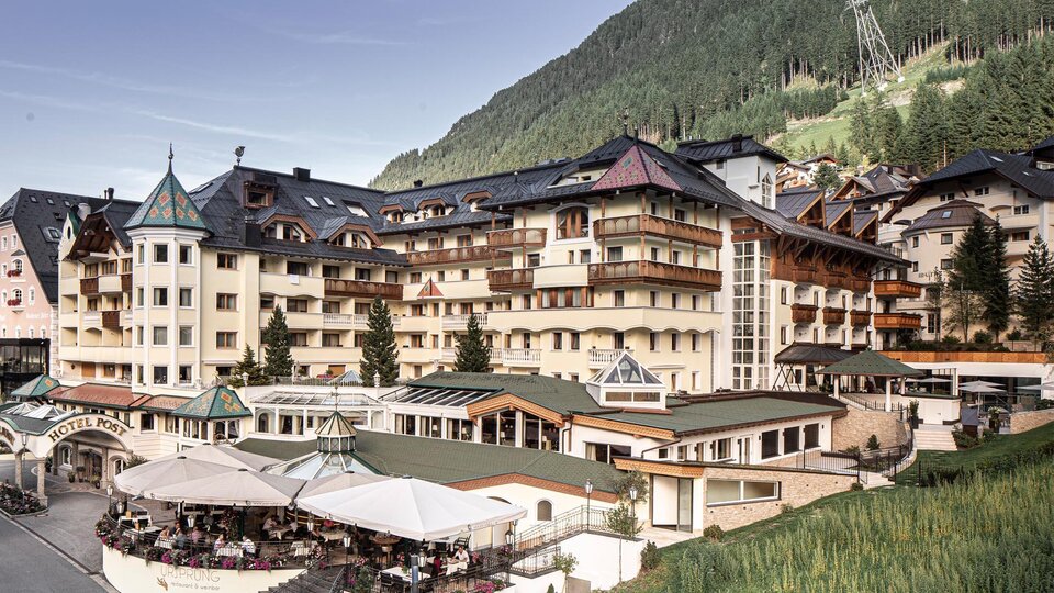 A modern hotel in the mountains with an inviting terrace. The surroundings are green and the architecture blends tradition with contemporary design.