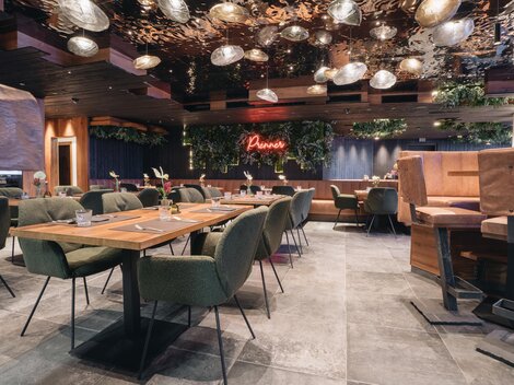 A modern restaurant with cozy tables and stylish chairs. The lighting and plants create an inviting atmosphere.