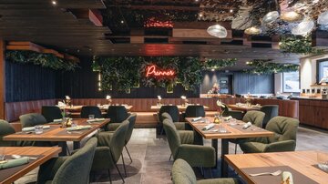 A modern restaurant with elegant tables and chairs. The room is decorated with plants and a bright neon sign.