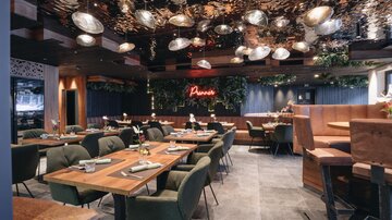 A modern restaurant with stylish wood and green tones. The tables are elegantly set and a cozy atmosphere is created by the lighting.
