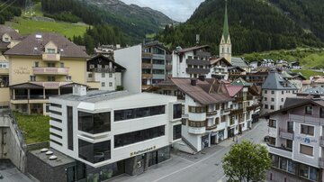 A modern building in a picturesque village view. Surrounded by traditional houses and mountains in the background.