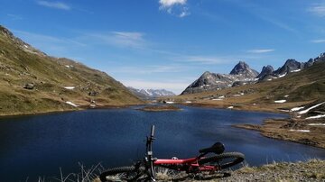 A breathtaking landscape with a clear lake and mountains in the background. A bicycle is lying on the shore of the lake.