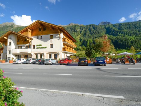 A beautiful hotel with traditional architecture is located by the roadside. In the background, green mountains and trees can be seen.
