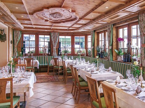 An elegant restaurant with wooden furniture and a cozy atmosphere. The tables are festively decorated with glasses and flowers.