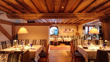 A cozy restaurant with a wooden ceiling and warm lighting. The tables are elegantly set and invite you to linger.