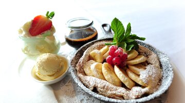 A delicious dessert plate with an apple-banana casserole, garnished with fresh berries and mint. Accompanied by ice cream and a sweet sauce.