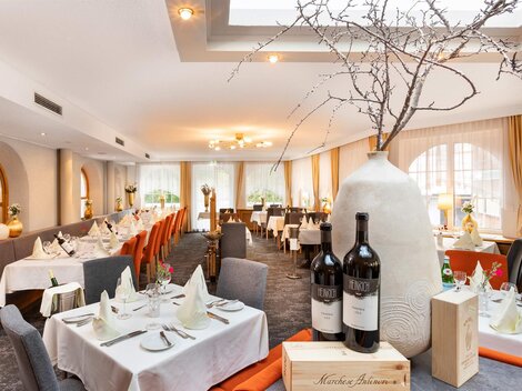 An elegant restaurant with set tables and stylish decoration. A large, decorative jug stands in the foreground next to two bottles of wine.