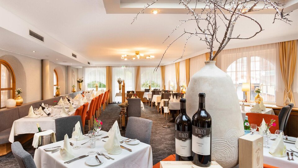 An elegant restaurant with set tables and stylish decoration. A large, decorative jug stands in the foreground next to two bottles of wine.