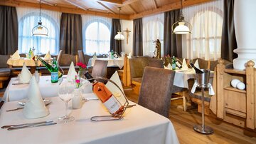 An elegantly furnished restaurant with wood-paneled walls and cozy tables. The tables are set with white tablecloths and decorative napkins.