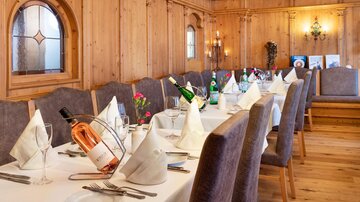 An elegant dining room with wooden paneling and a long table set for a festive dinner. On the table, there are wine bottles and decorative napkins.