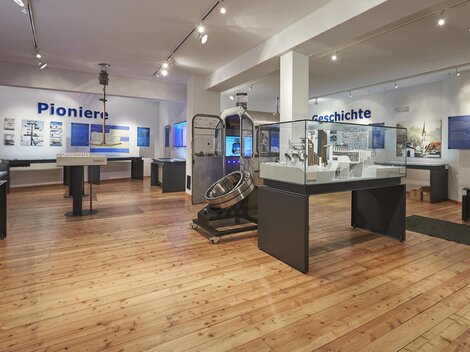 Ein modernes Ausstellungszimmer mit Holzboden. Vitrinen und Informationen über Pioniere und Geschichte sind an den Wänden angebracht.