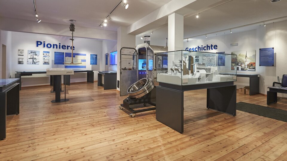 Ein modernes Ausstellungszimmer mit Holzboden. Vitrinen und Informationen über Pioniere und Geschichte sind an den Wänden angebracht.