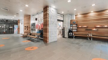 A modern reception area with wooden paneling and gray tiles. Some benches and display shelves are visible.