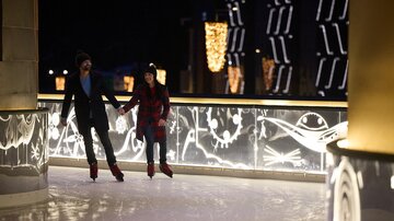 A couple walking hand in hand on an ice rink. The surroundings are festively lit.