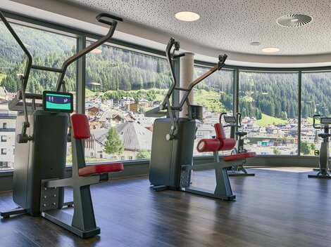A modern gym with equipment and large windows that offer a view of the mountains. The rooms are bright and invite you to work out.