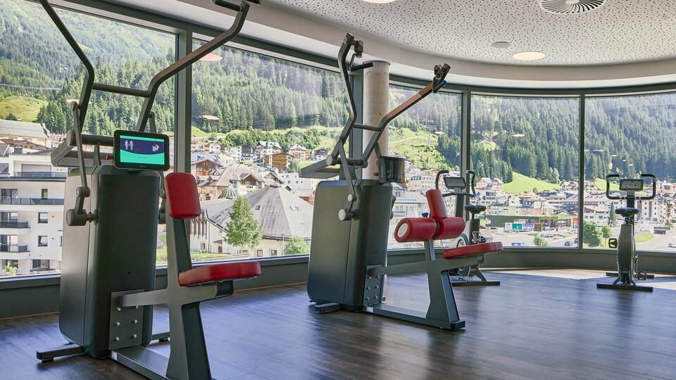 A modern gym with equipment and large windows that offer a view of the mountains. The rooms are bright and invite you to work out.