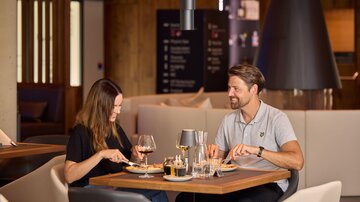 Ein Paar genießt ein romantisches Abendessen in einem modernen Restaurant. Sie sitzen an einem Tisch mit Getränken und Essen.