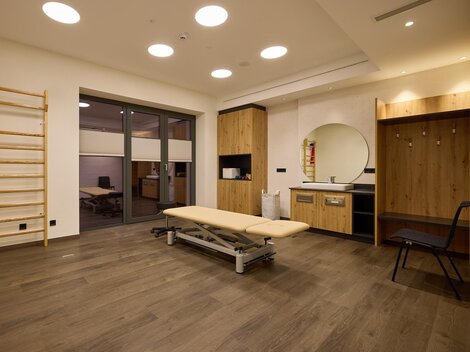 A bright, modern therapy room with a treatment table and a wall with various training equipment. There is a mirror and wooden shelves that create an inviting atmosphere.