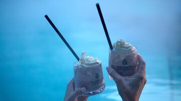 Two cocktails with cream in hand, held over a blue pool. The relaxed atmosphere invites enjoyment. | © Silvrettaseilbahn AG
