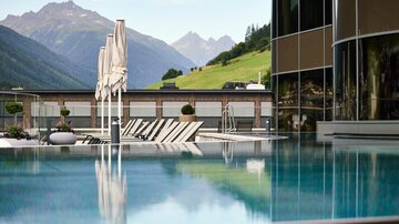 A beautiful infinity pool overlooking green mountains. Umbrellas and loungers invite you to relax.