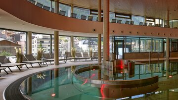 A modern spa with a clear swimming pool and comfortable loungers.  
Wide windows offer a beautiful view of the surroundings.