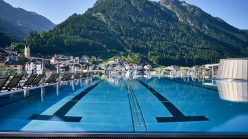 A stylish infinity pool overlooking green mountains. In the background, a picturesque town can be seen.