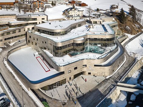 A modern building in a snow-covered landscape with an ice rink accessible all year round. The architecture is elegant, surrounded by picturesque mountains and vacation homes.