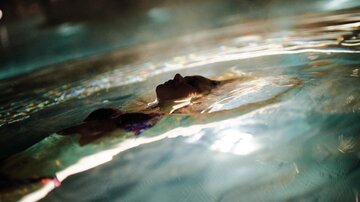 A person swims relaxed in the water and looks up. The gentle waves reflect the light.