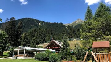 A beautiful landscape with mountains and dense forests. In the foreground, there is a garden café and a playground.