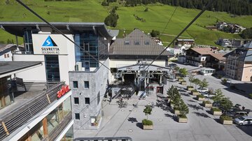 A modern lift area with a large building in the background. The surroundings are green and provide a cozy atmosphere.