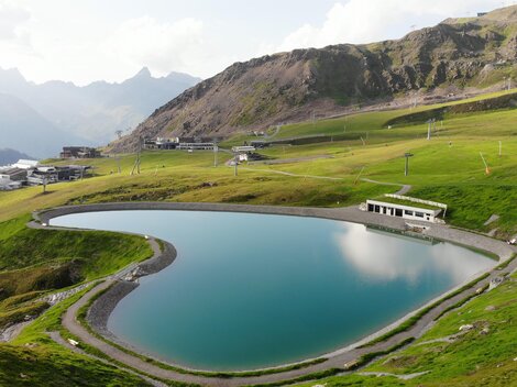 A picturesque mountain lake surrounded by green meadows and high mountains. The water's surface reflects the landscape.