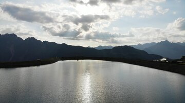 A tranquil mountain lake with sparkling water and majestic mountains in the background. The cloudy sky creates a moody atmosphere.
