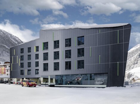 A modern hotel building in a snow-covered mountain valley. The facade is stylish and eye-catching, surrounded by a wintry landscape.