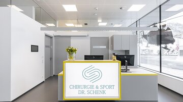 A modern reception area with a bright, welcoming reception desk. Large windows let in plenty of daylight and offer a view outside.