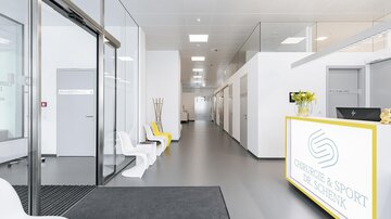 A modern reception area with a bright, minimalist design. On the right side, there is a reception desk featuring the name of the facility.
