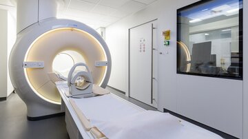 A modern MRI room with a large machine and a transparent window. The walls are light, and the room appears clean and well-organized.