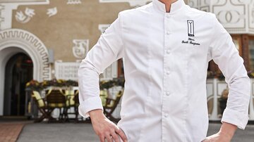 Ein Koch steht selbstbewusst vor dem Gasthof Yscla. Der Hintergrund zeigt die gut dekorierte Fassade des Restaurants.