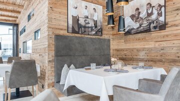 A stylish restaurant with wooden paneling and modern furniture. The walls are decorated with artworks depicting historical scenes.